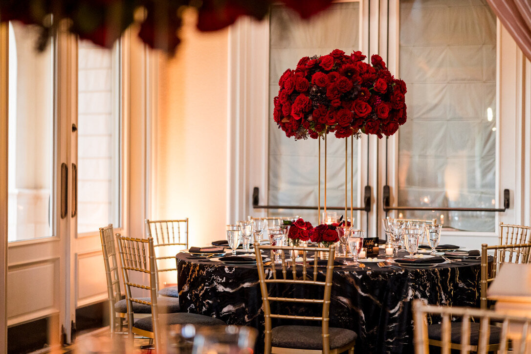 black and gold linen, gold four prong stand, red flowers, red roses, chocolate hydrangea, gold chairs,