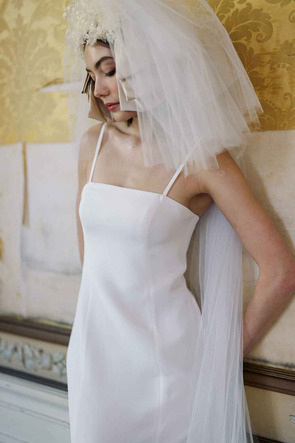 bride in wedding dress and veil leaning against wall