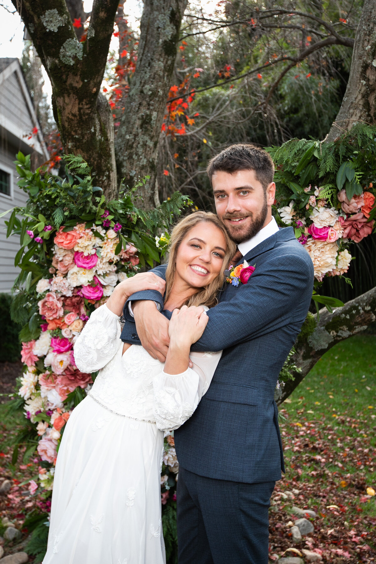 A bride and groom embrace in front of a tree covered in bright flowers