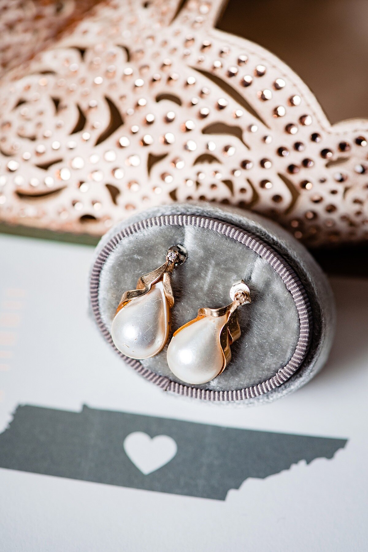 Detail photo of the pearl and gold earrings the bride will wear on her wedding day as well as her ivory filigree patterned leather heels. The state of Tennessee with a heart over Murfreesboro in gray.