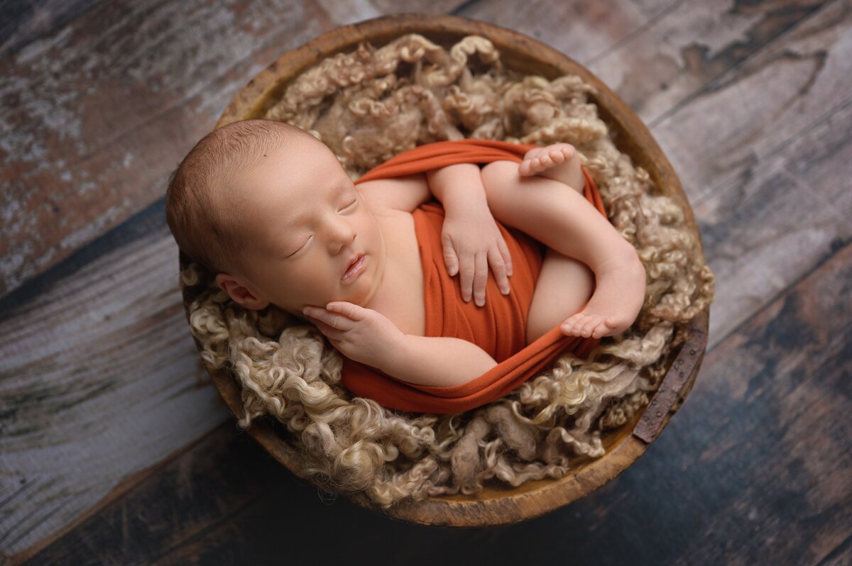 Baby in orange wrap posed in a prop with gorgeous lighting.