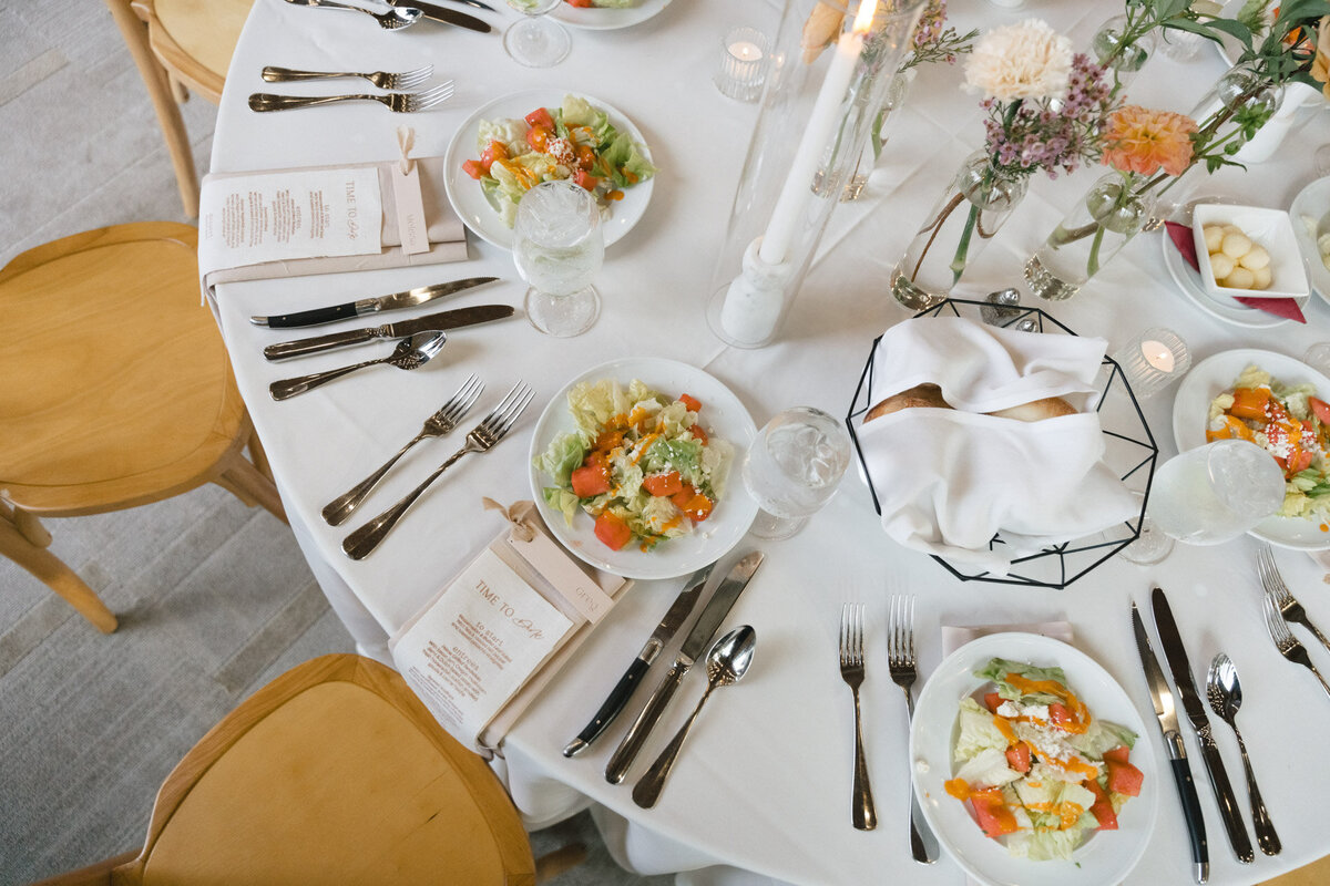 custom calligraphy wedding menu with flatware placed on a napkin on a wedding tablesetting with plated salad representing full service design and calligraphy by Life in Letters.