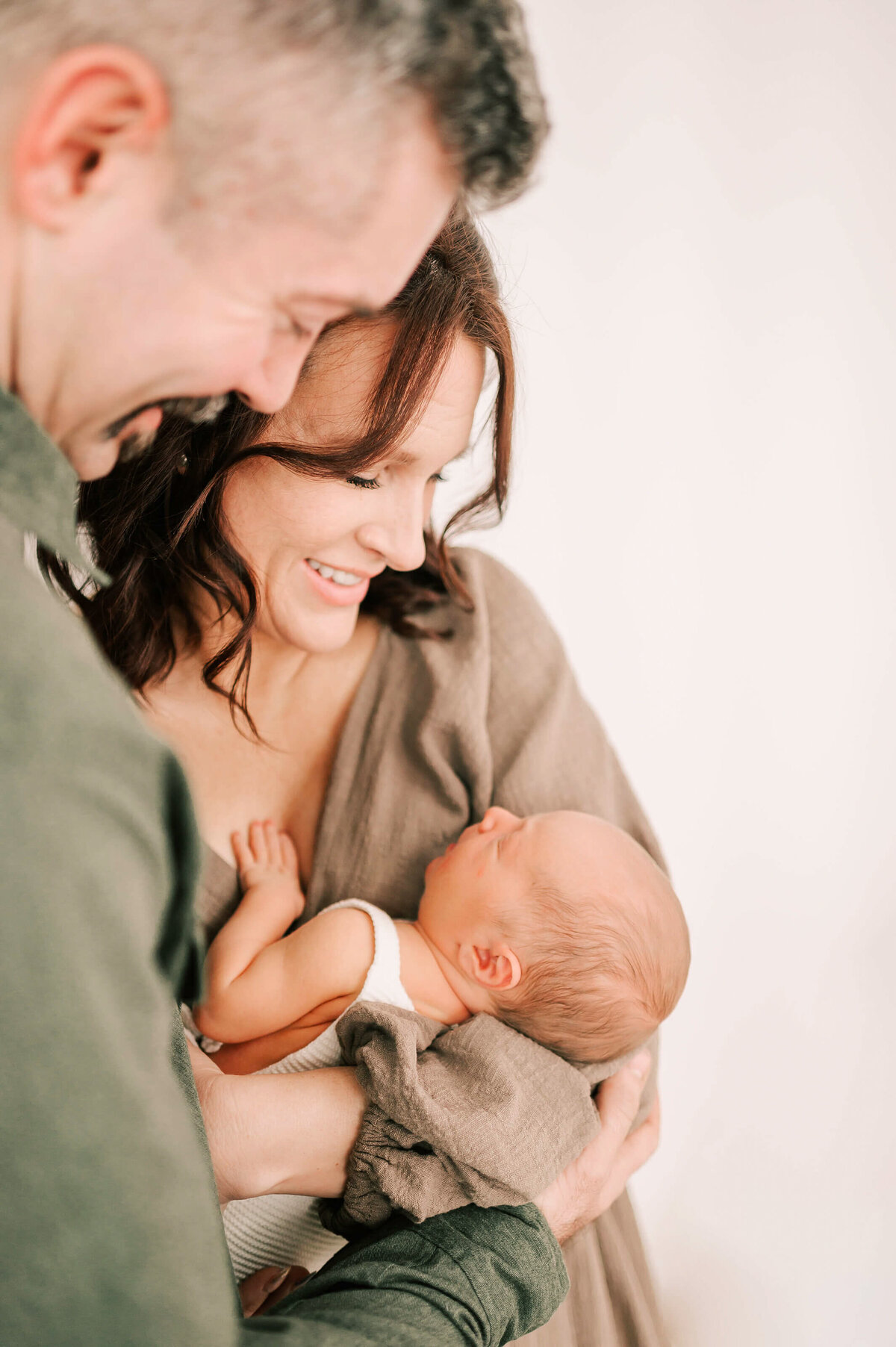 newborn photo of parents smiling down and holding newborn boy in photography studio in Springfield MO