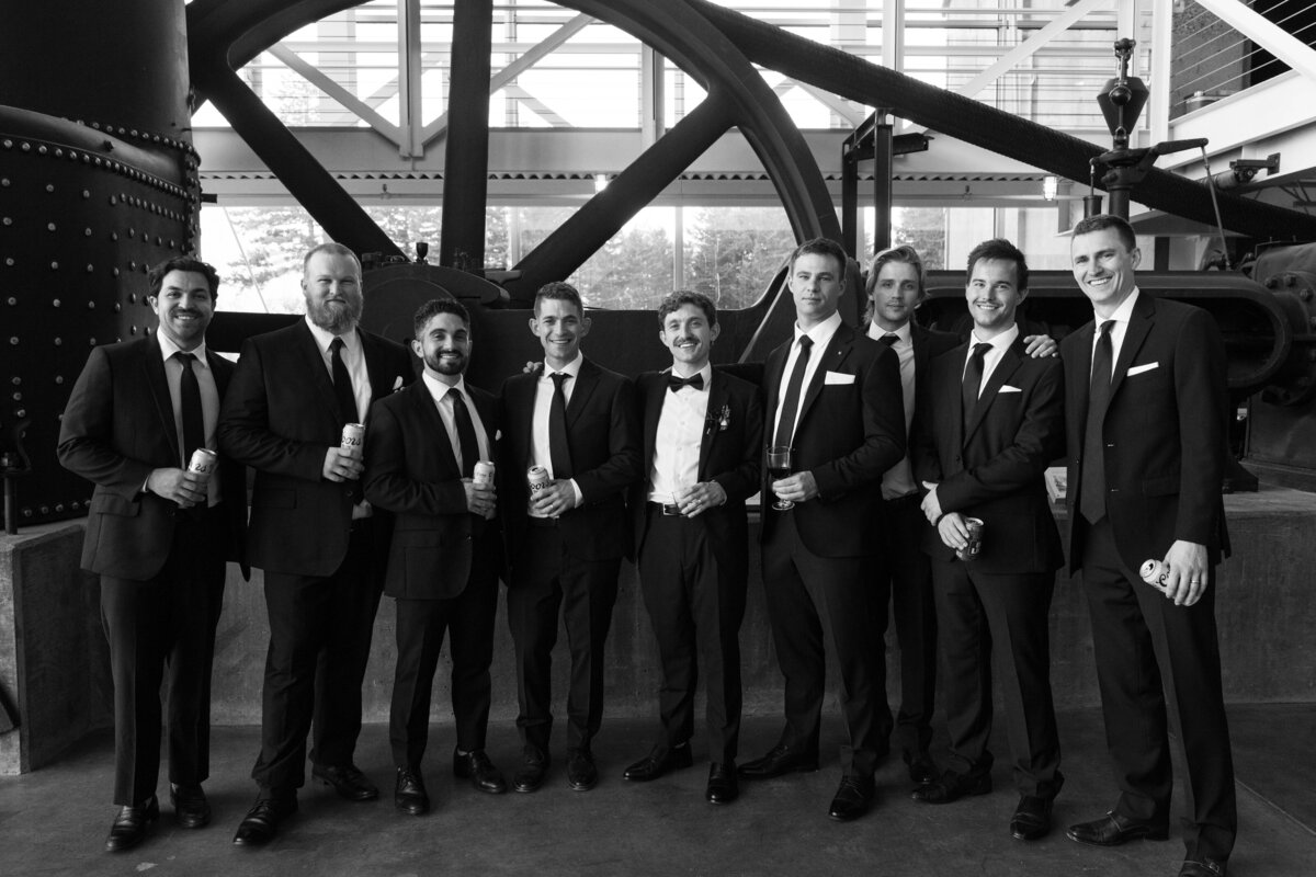 Groom with groomsmen in black tuxedos posing at modern industrial wedding venue