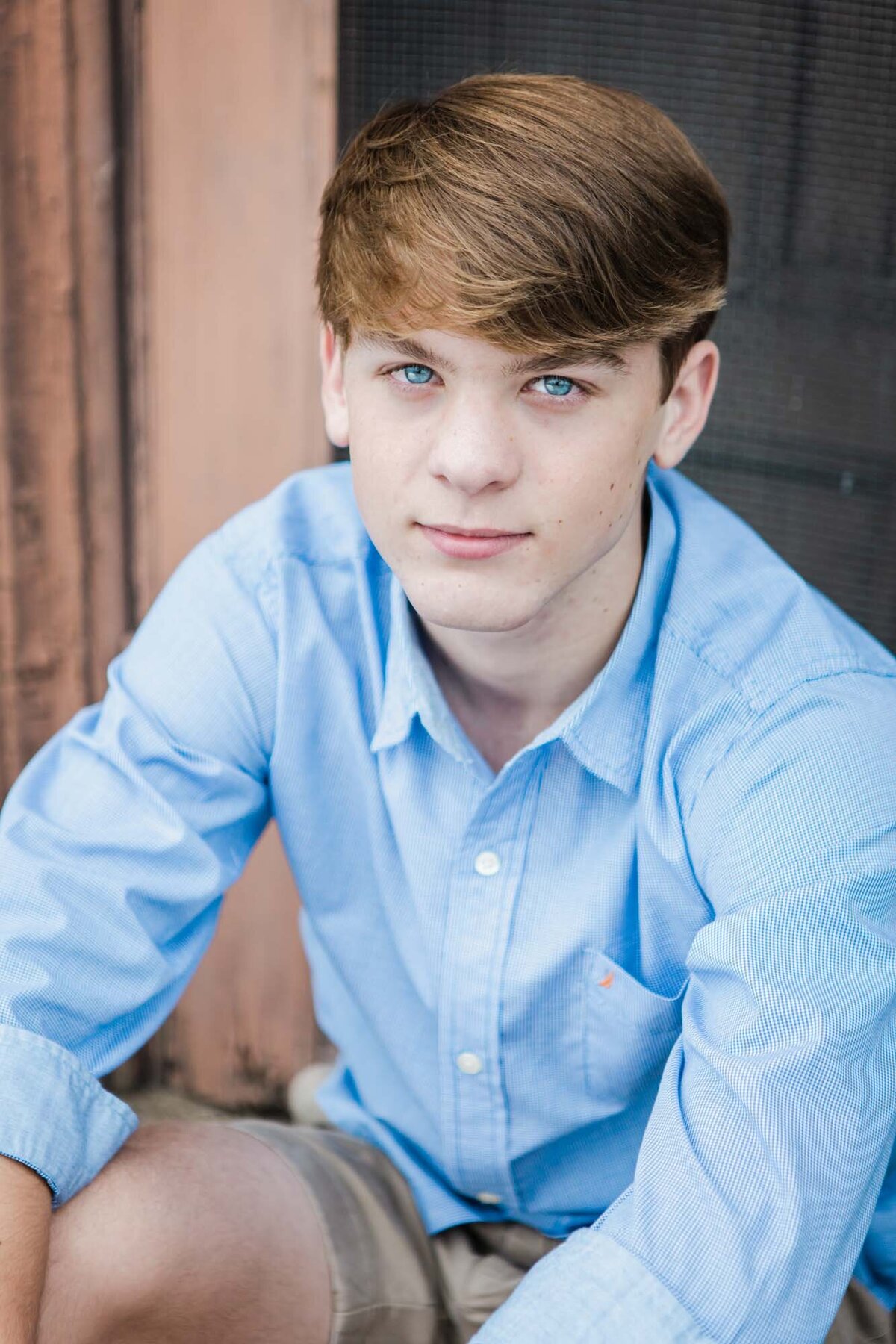 Senior with blue eye and shirt sitting on the stoop of a doorway.