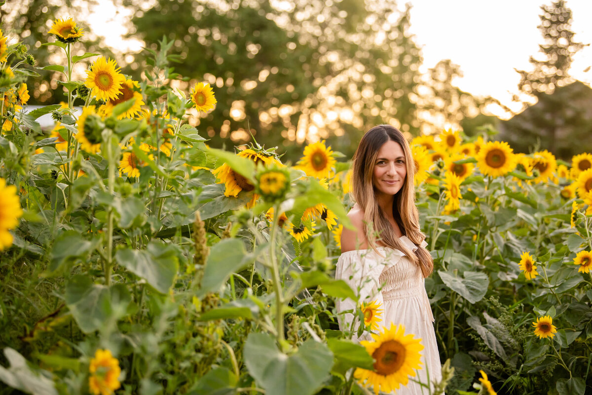 mom wearing a beige dress standing in the sunflower field for her family photos