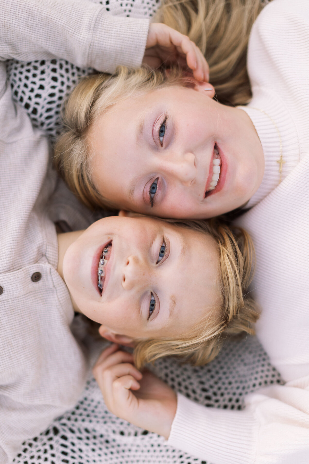 brother and sister siblings lay on a blanket and smile side by side