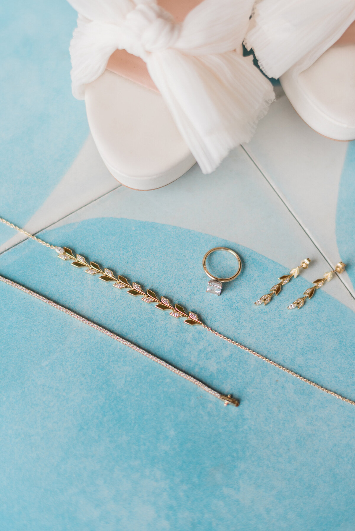 Bride's jewelry sits next to white heels 