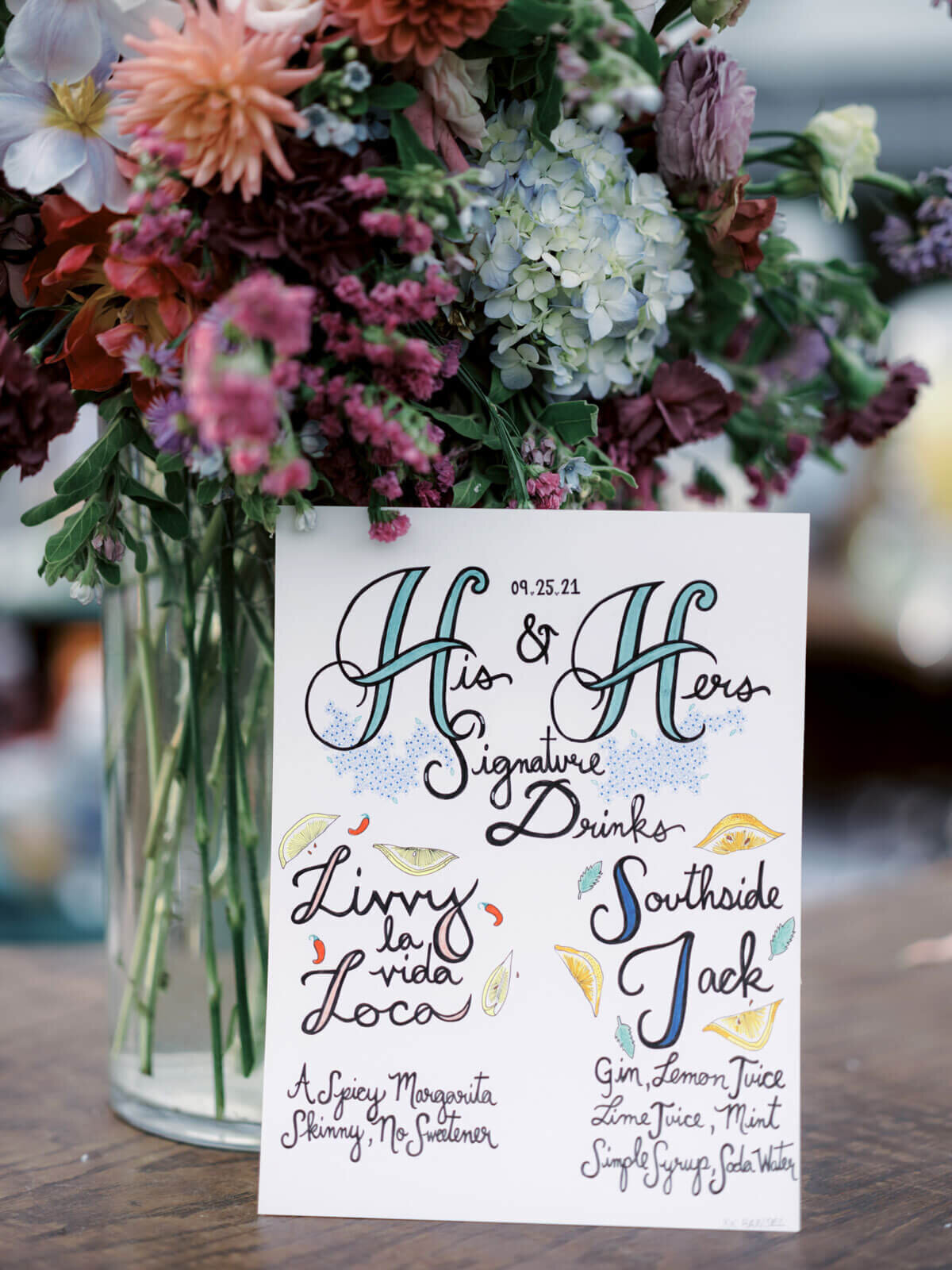 A close-up shot of the wedding drinks menu with pretty flowers on a table at The Ausable Club, NY. Image by Jenny Fu Studio.