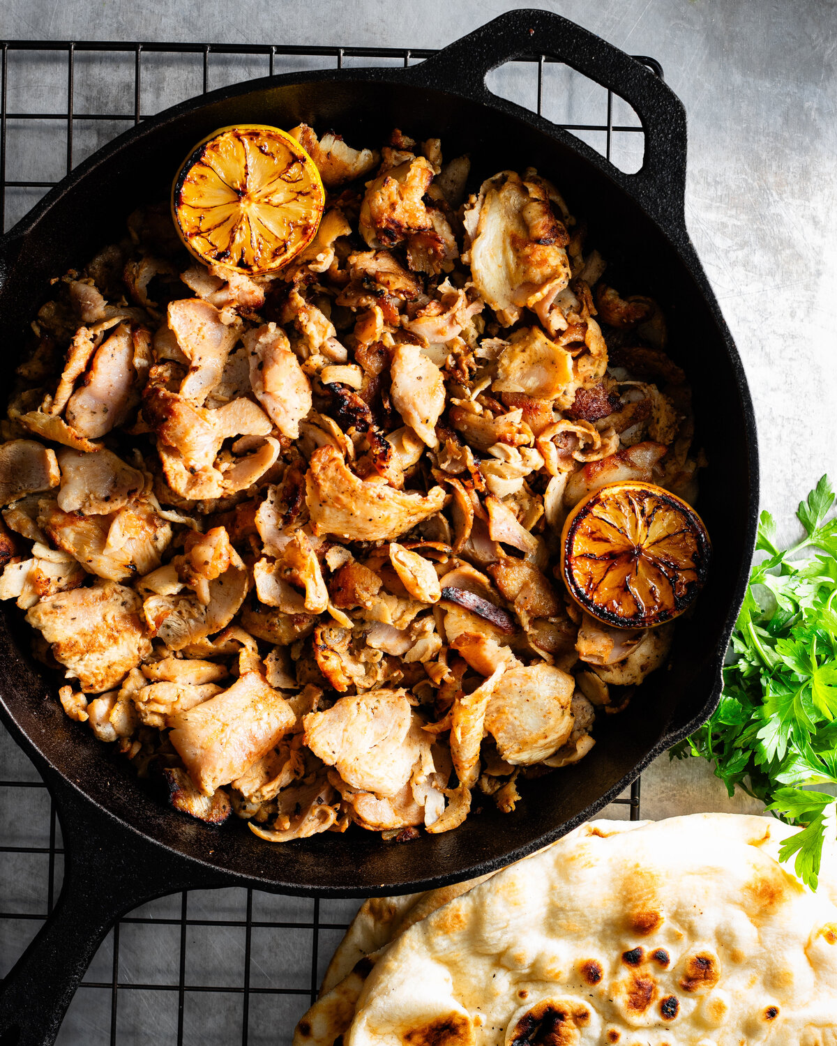 A cast iron frying pan filled with chicken gyros with burnt lemon and pitta bread
