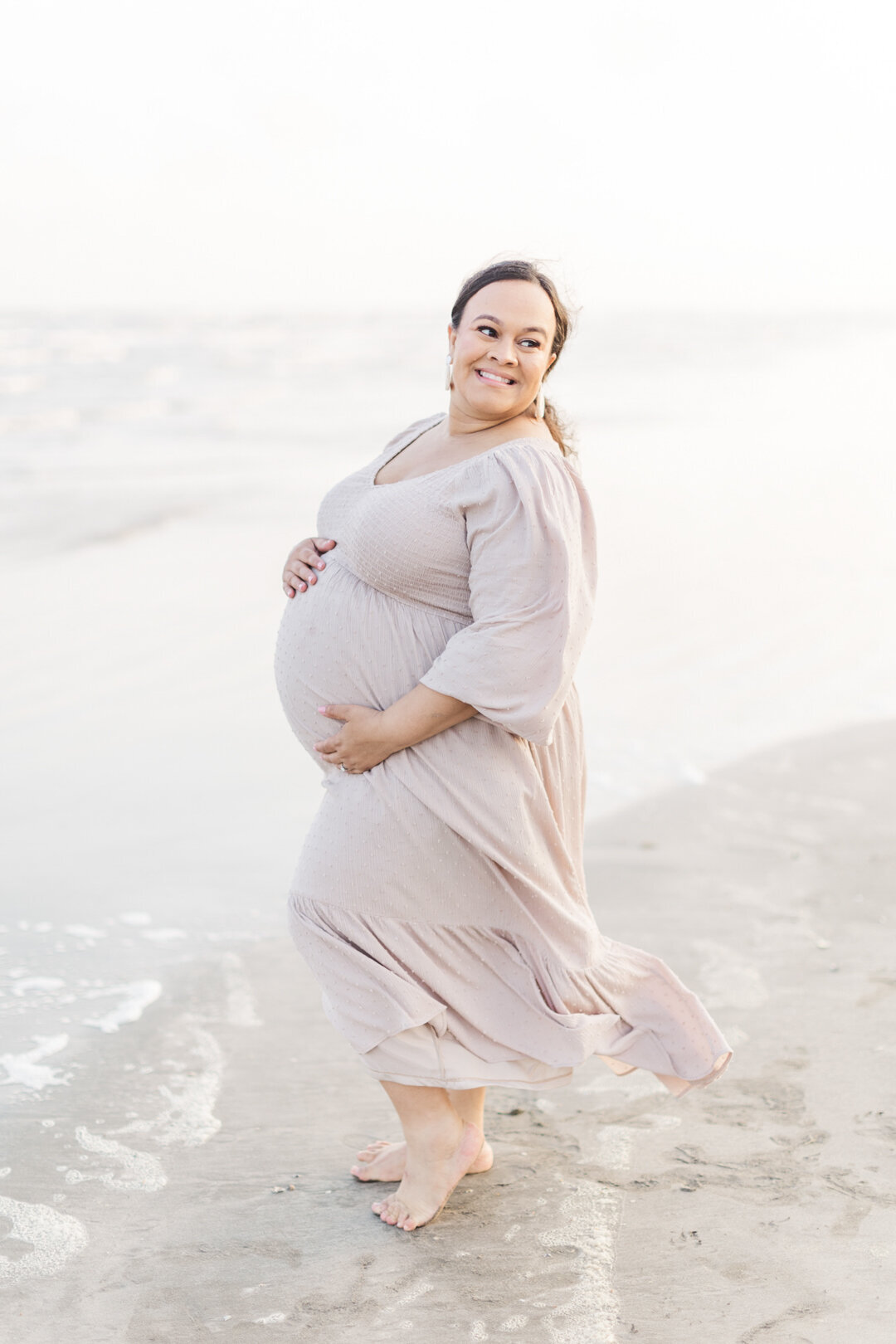 mom holds belly smiling behind her shoulder for galveston photo session