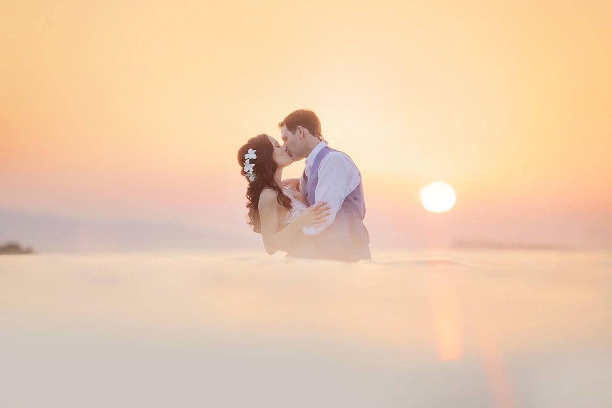 Woman wearing a flower in her hair kisses her husband in the ocean after he proposes on Maui with Love + Water