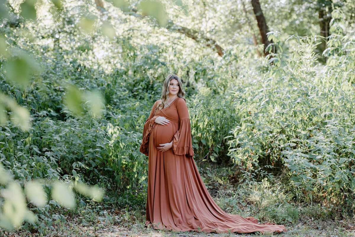pregnant mother standing in field in long orange dress