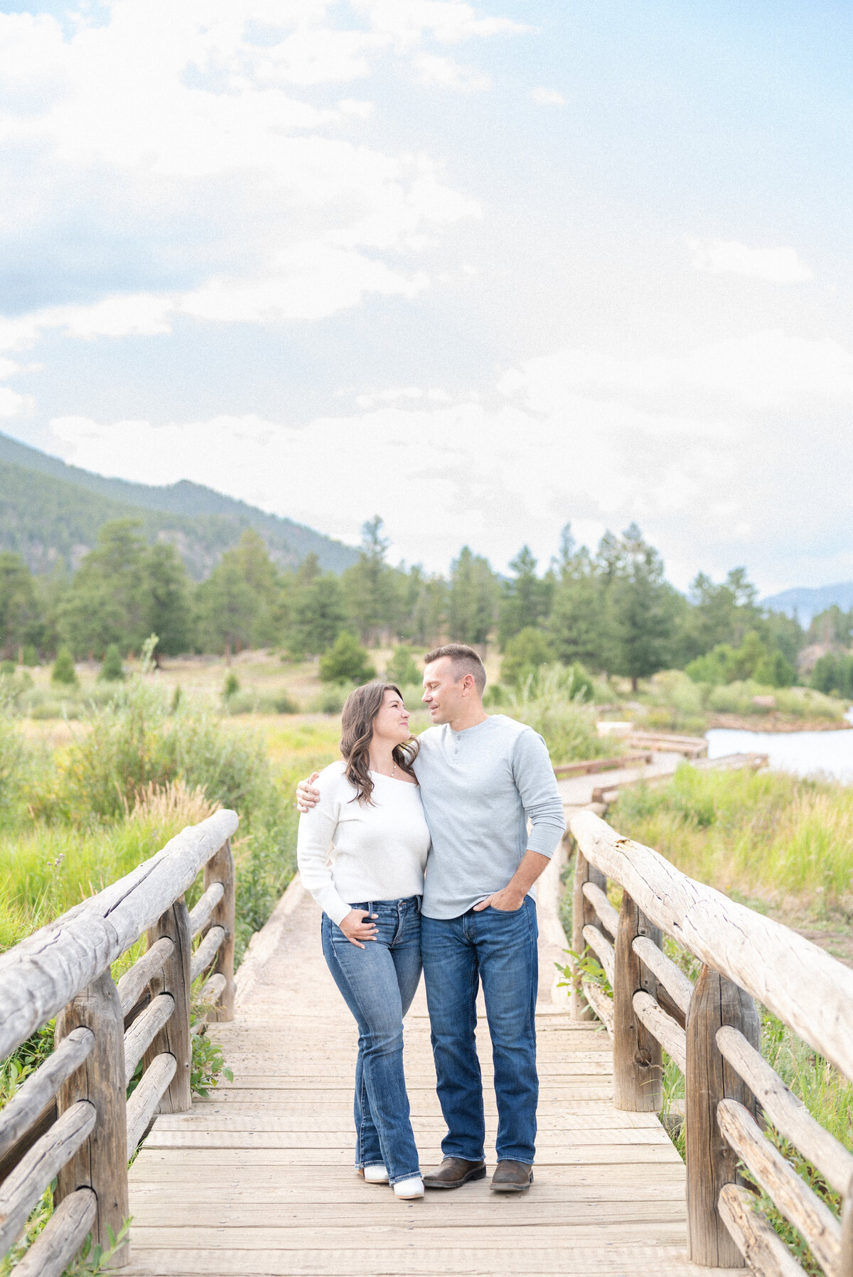 Couple sharing side hug while looking at each other standing on a wooden bridge in rocky mountain national park