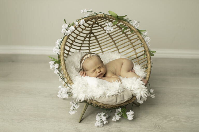 Newborn baby girl peacefully sleeping in a wicker basket, nestled in soft blankets, creating a warm and cozy portrait
