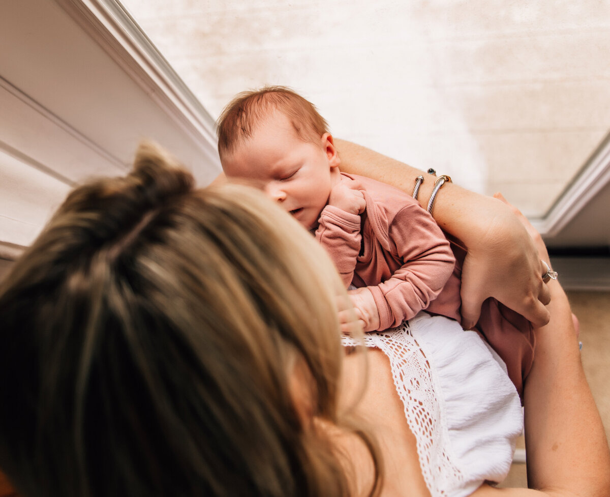 Newborn Photographer, Mom holding baby while standing next to the window.