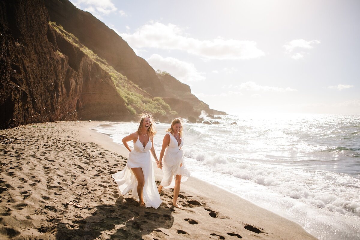 A same sex lesbian couple runs along the beach in Hawaii on  their wedding day