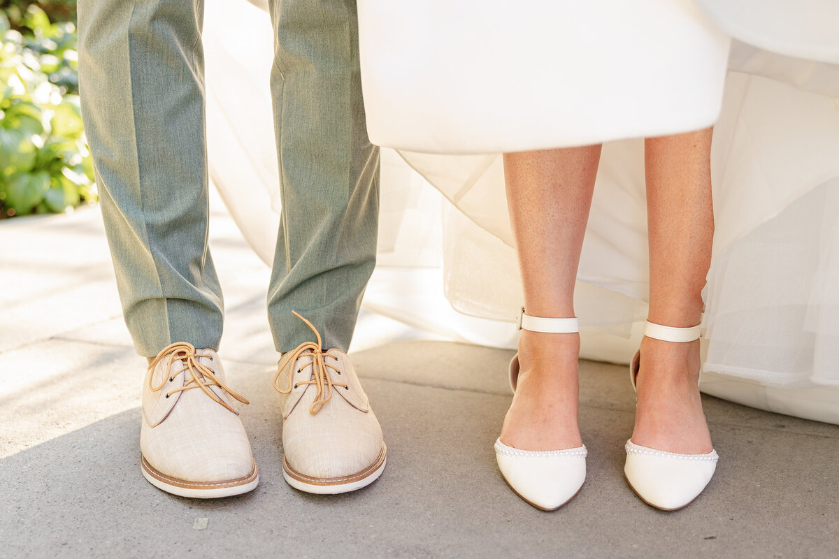 A stylish shot of the couple’s footwear, with the groom wearing beige lace-up shoes and the bride in elegant white flats