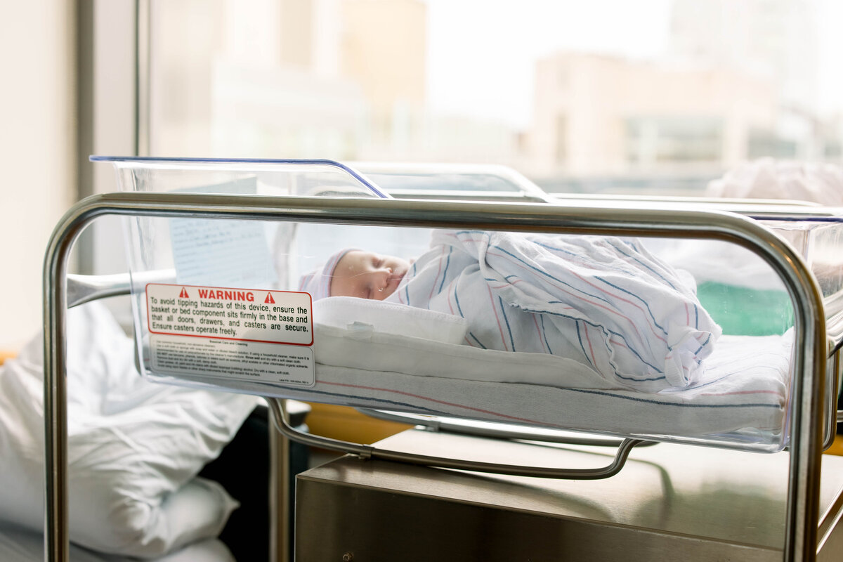 Baby in clear bassinet next to large window