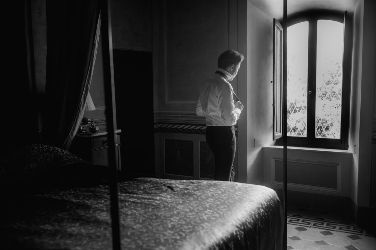 Getting ready picture of the groom in his hotel room in front of a open window.