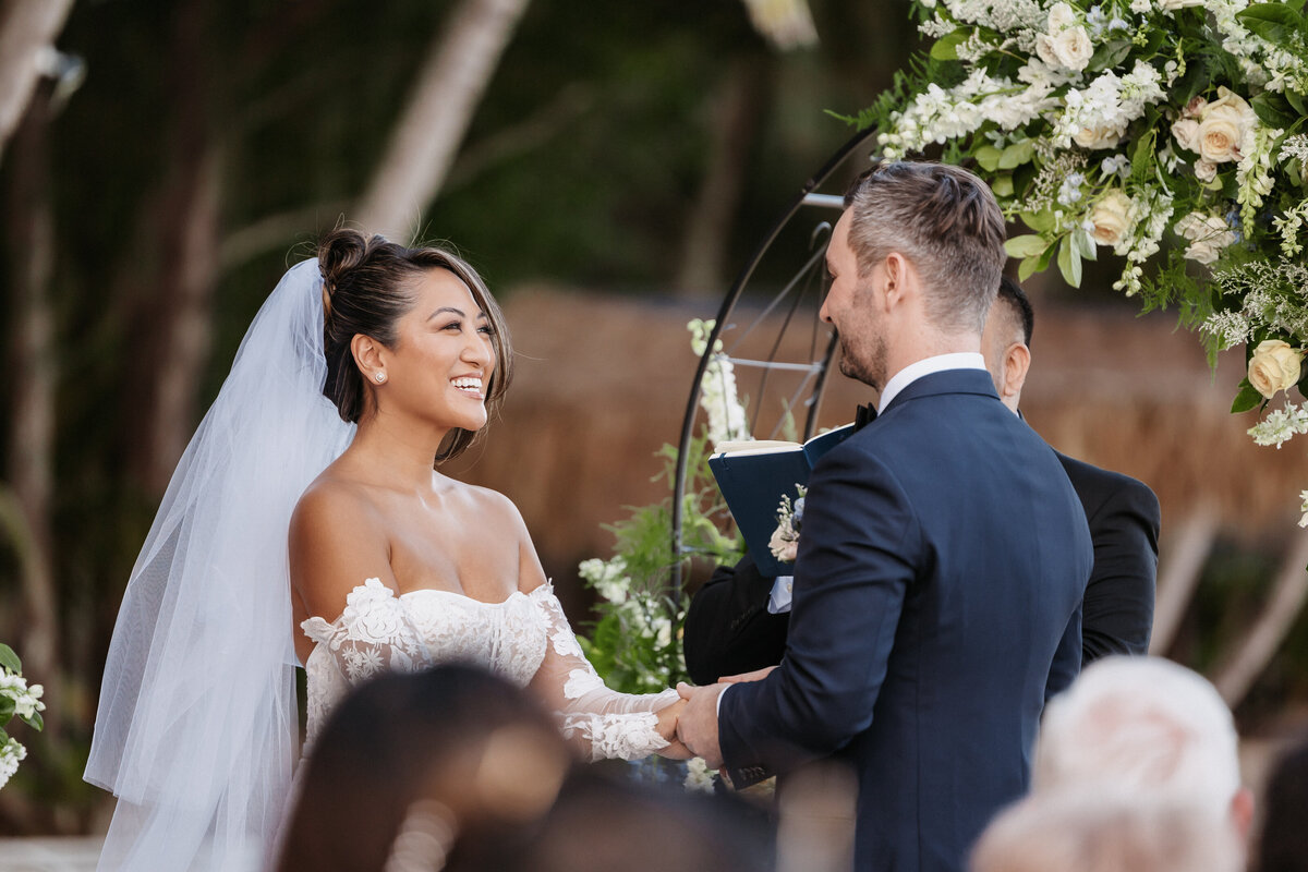Bride and groom ceremony at Kualoa Ranch on the beach, holding hands with palm trees and ocean in the background