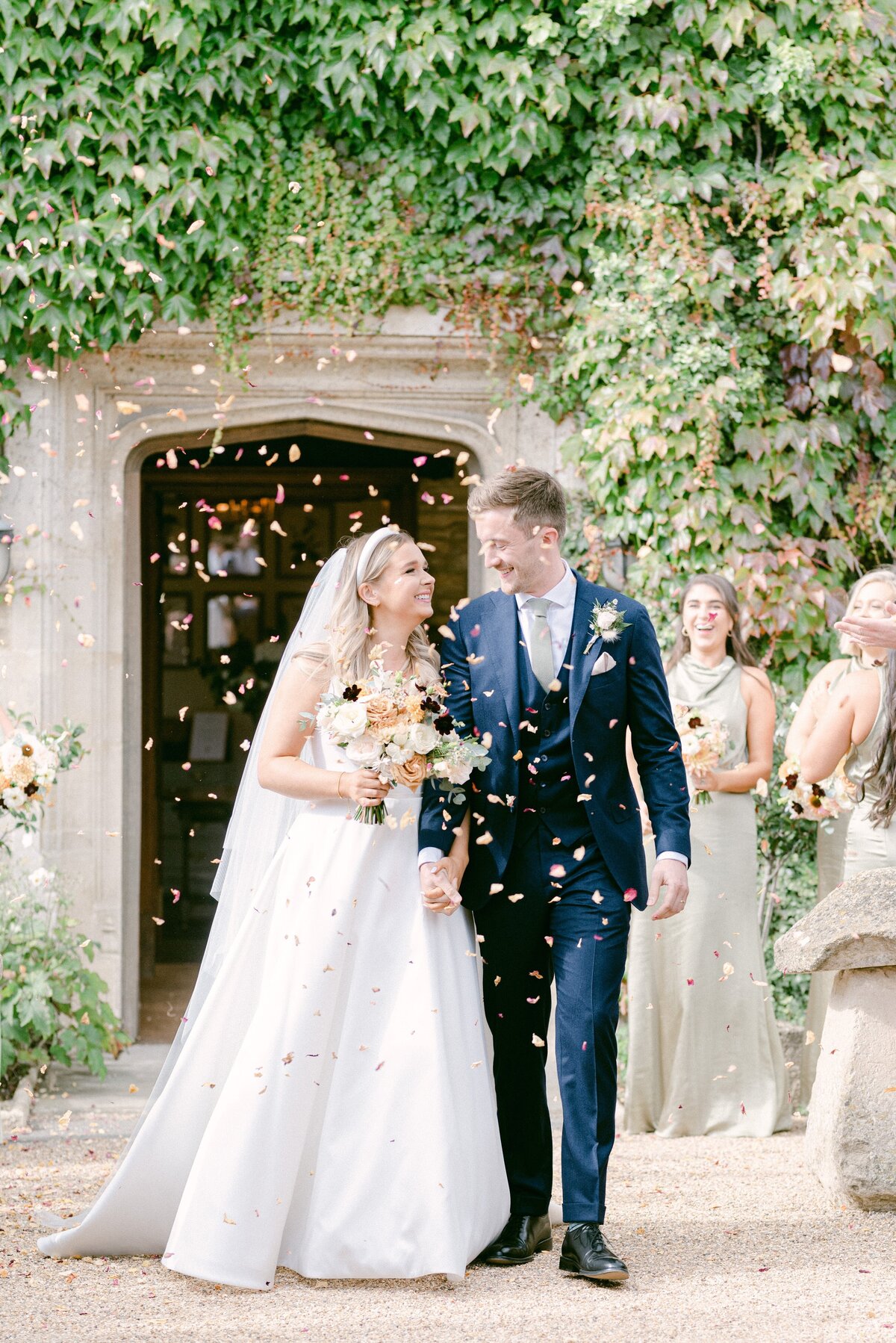 Surrey Wedding Photographer, Bride and groom walking down the middle of their guests who are throwing confetti over them at Hyde house in the cotswolds