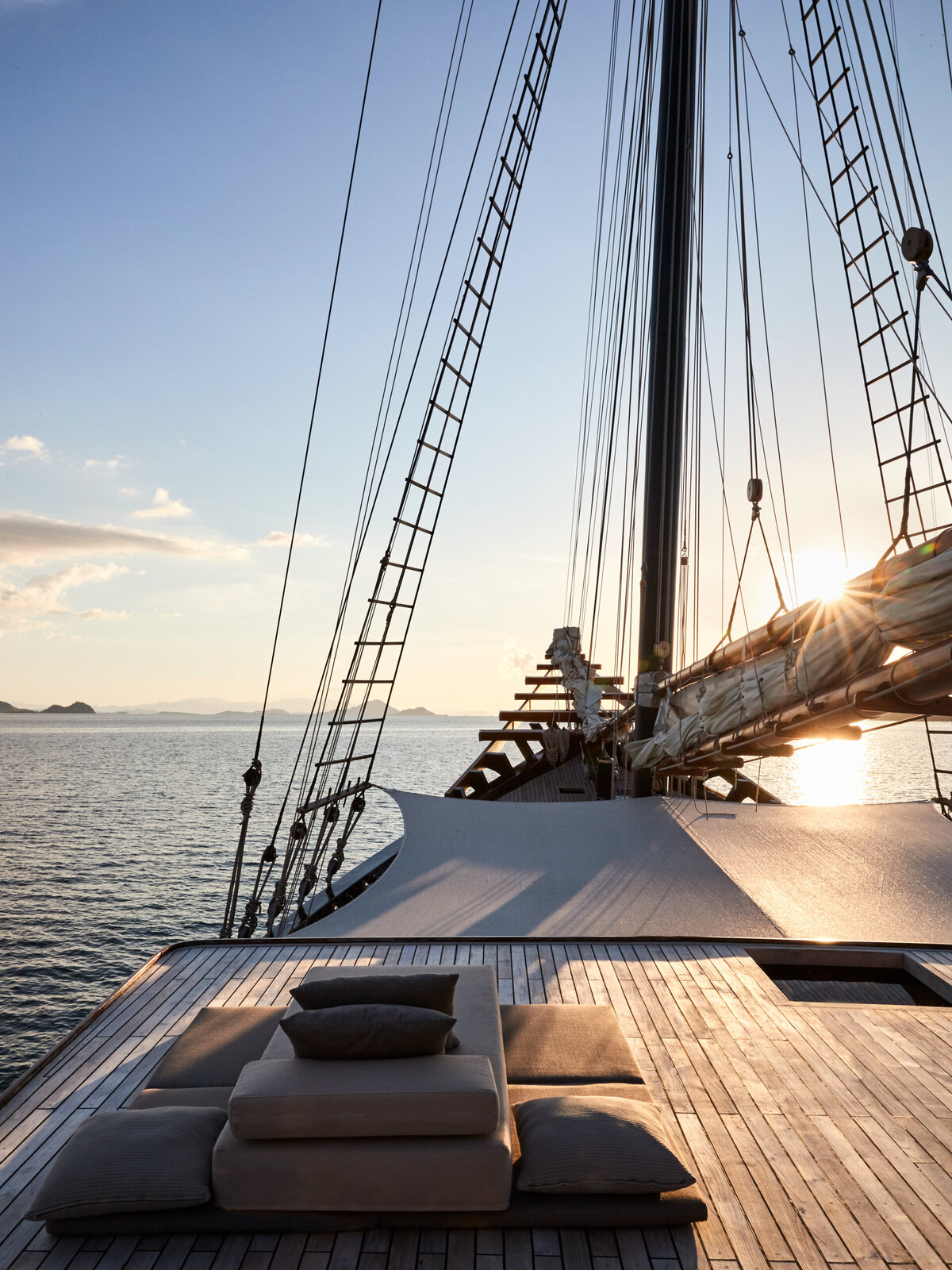 A serene sunset view from the deck of Amandira, a luxury private yacht in Indonesia, featuring plush lounge seating and open ocean views. 