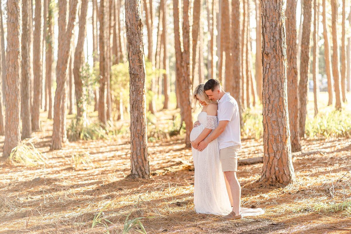 couple holding belly bump in pine forest maternity photoshoot in sunset
