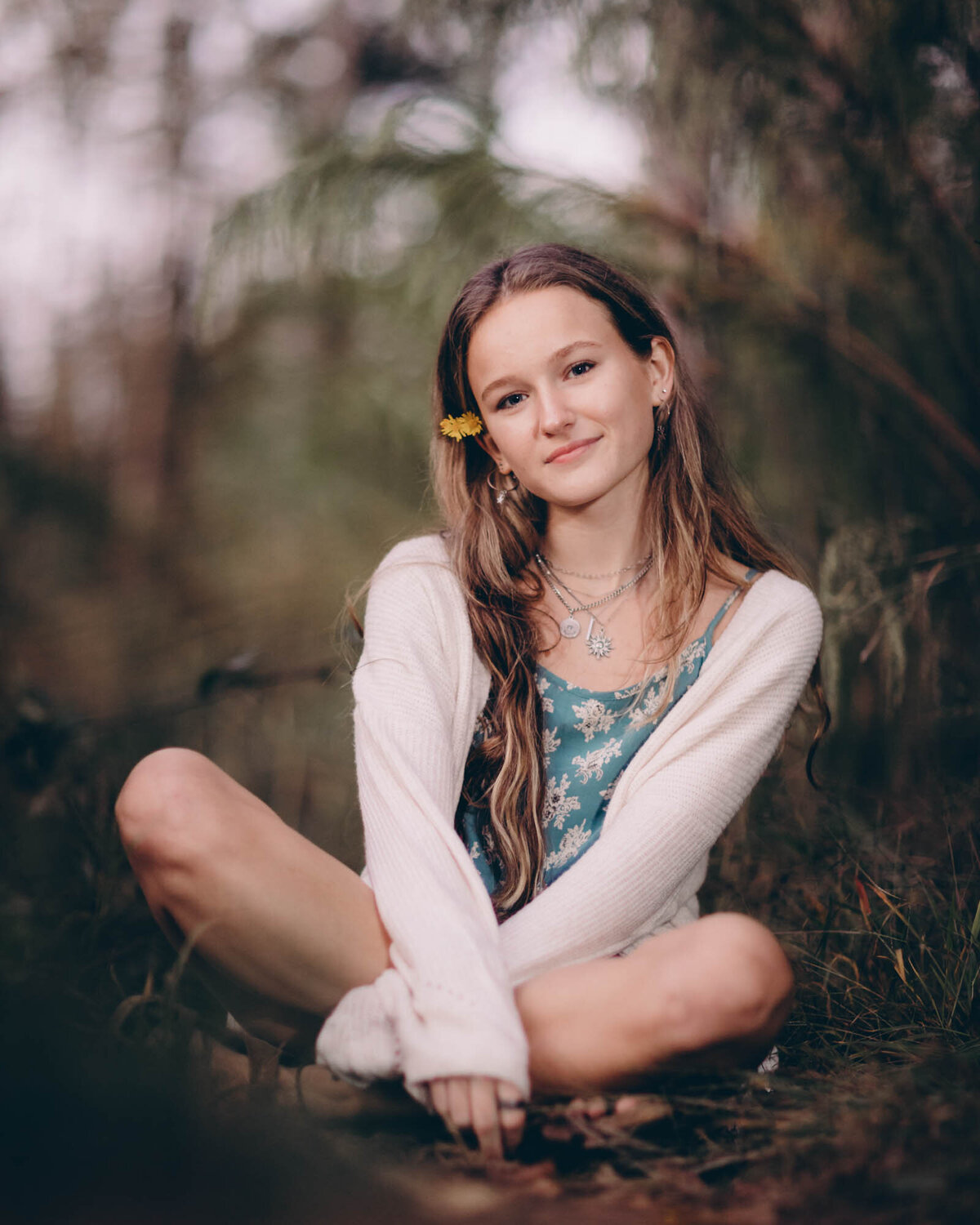 Gorgeous portrait of a girl sitting on the ground with a yellow flower in her hair.