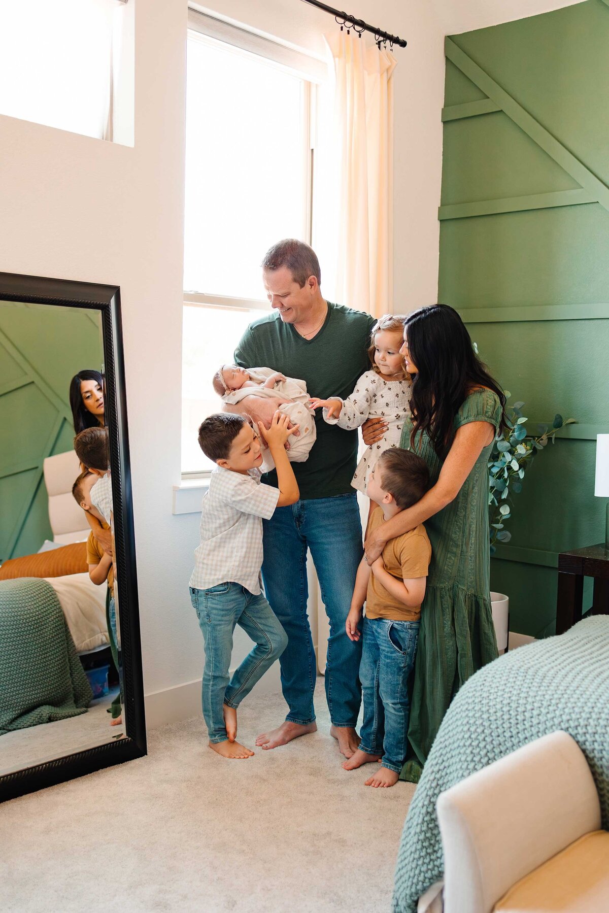 An amazing family enjoys a photography session with the best newborn photographer in Albuquerque. In a bedroom with green and cream decor, they wear elegant green outfits and jeans, expressing boho vibes.