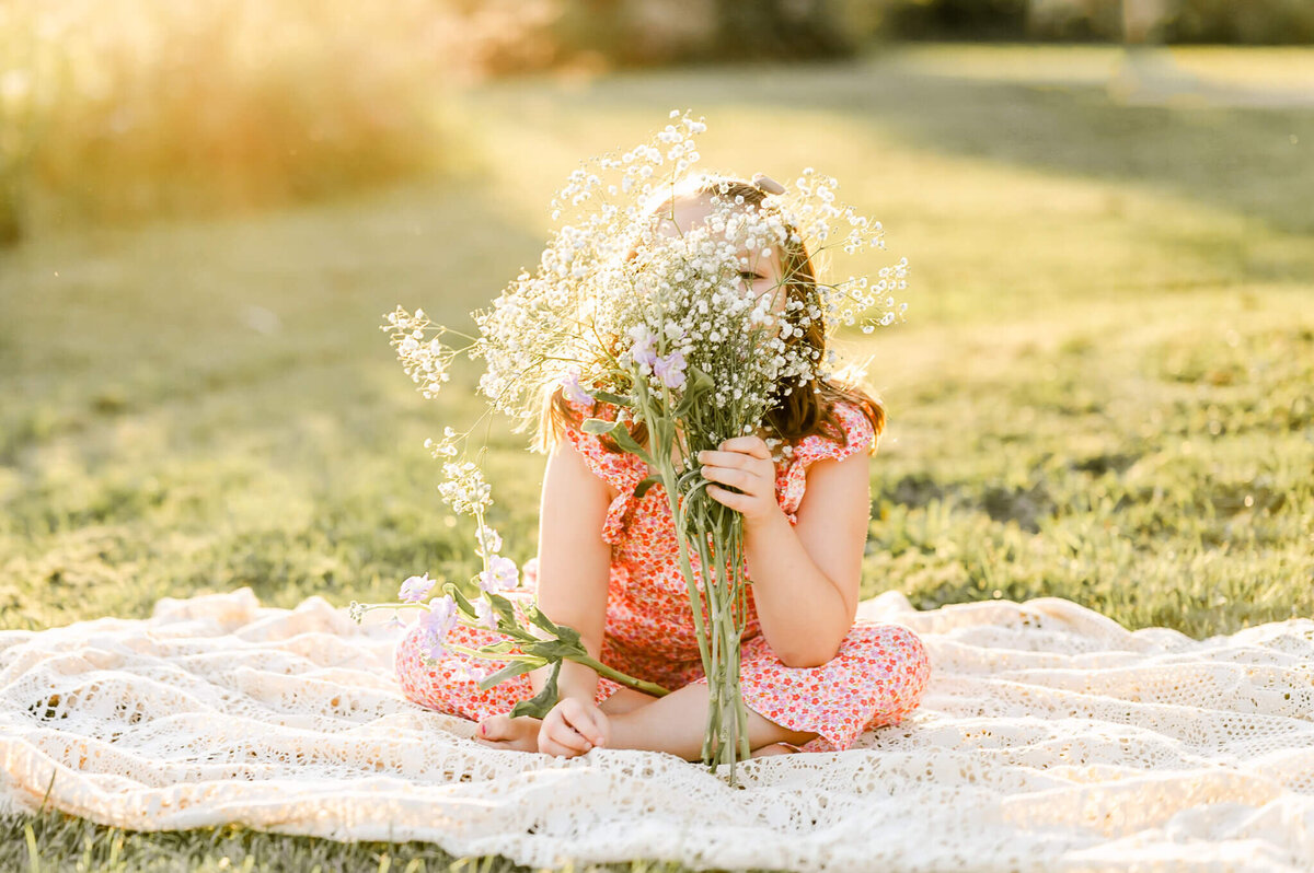 Young girl holding wildflowers while sitting on a blanket near Naperville, IL.