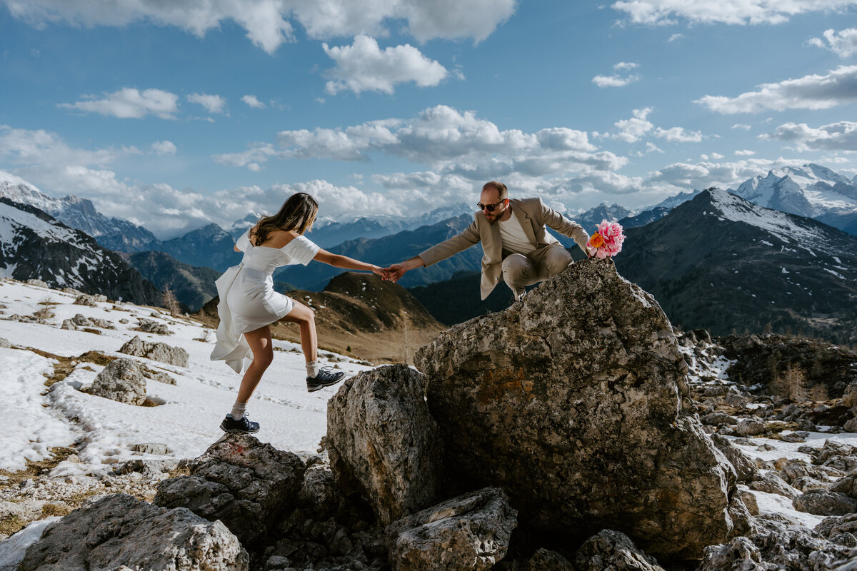 Bride reaching for groom’s hand while climbing rock during elopement
