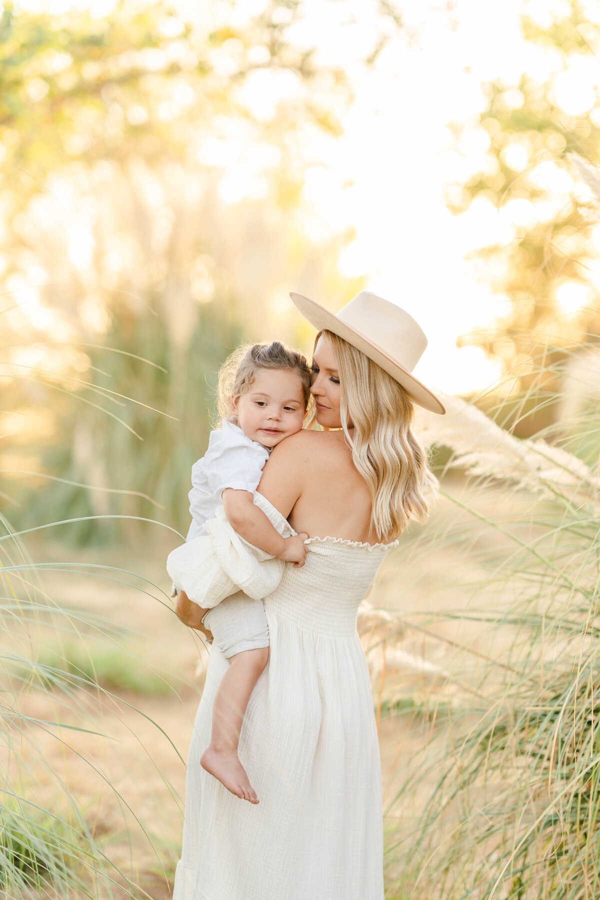A mother holds her son dressed in natural green tones standing in a pampas grass field photographed by Bay Area photographer, Light Livin Photography.
