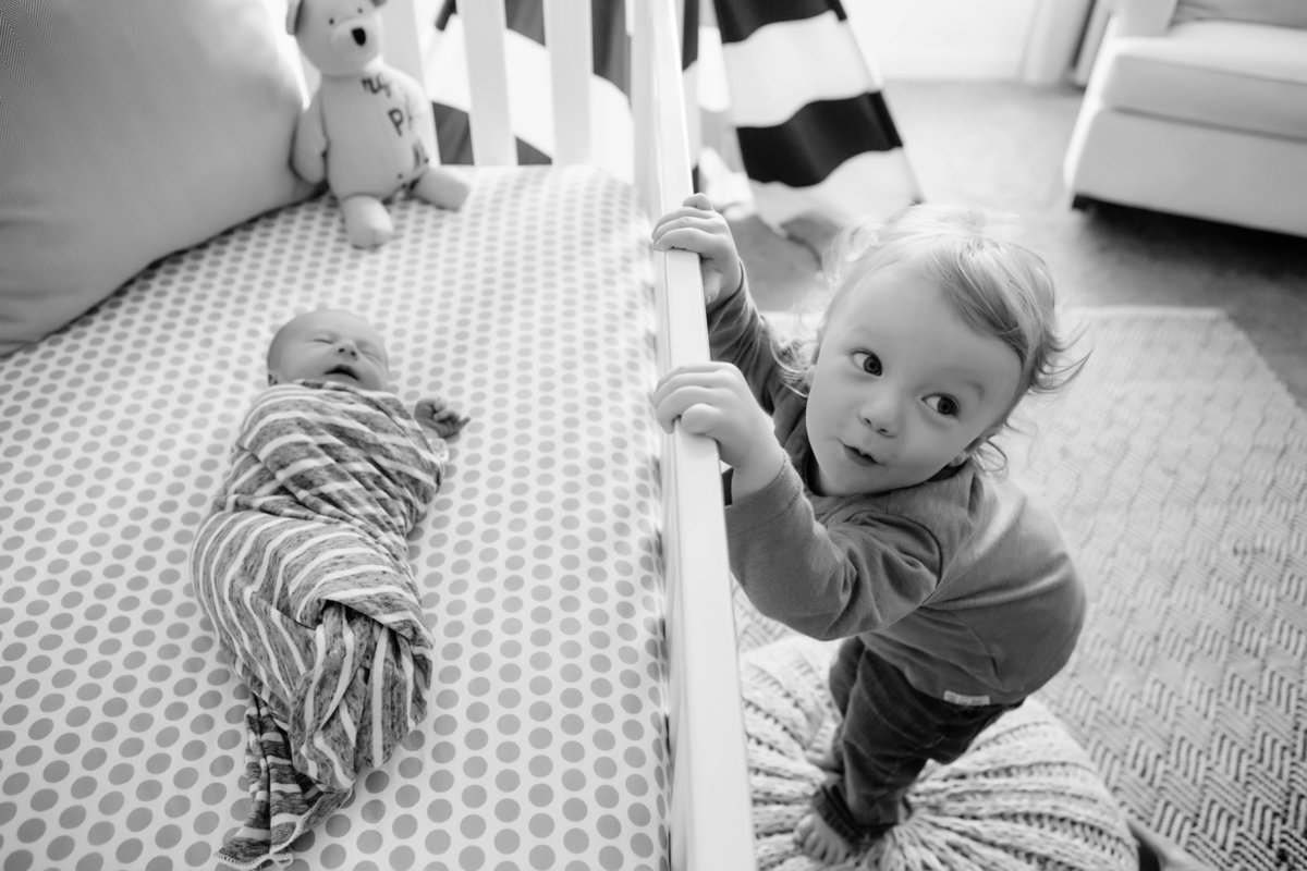 Toddler looking at baby in crib - Jen Madigan - Plainfield Lifestyle Newborn Photographer