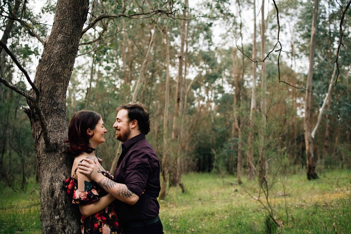 Woman leaning against tree, boyfriend leaning in to her, during couple photoshoot Melbourne, And So I Don't Forget Photography