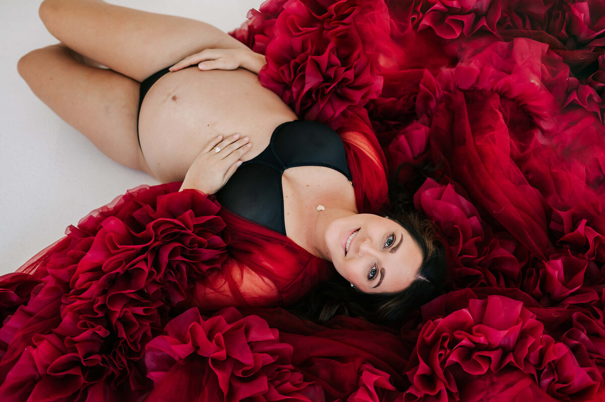 pregnant mom smiling laying on ground in maternity photography studio in Joplin MO