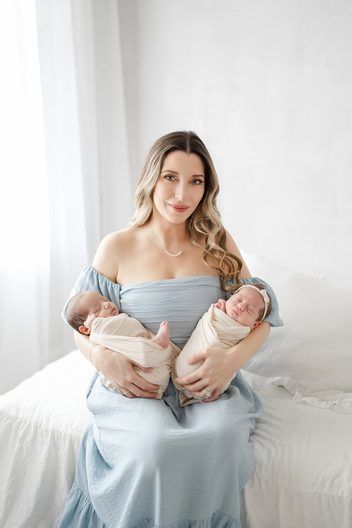 Timeless portrait of mother cradling newborn twins in soft neutral tones at luxury natural light studio in Tampa