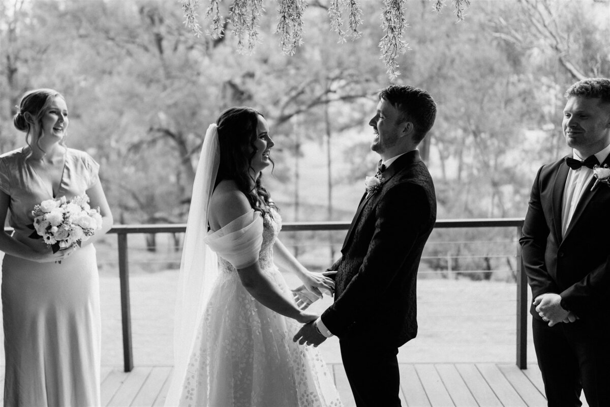A radiant bride, clutching a bouquet of ivory roses, exchanges heartfelt vows with her groom under a cascading arch of fragrant blooms.