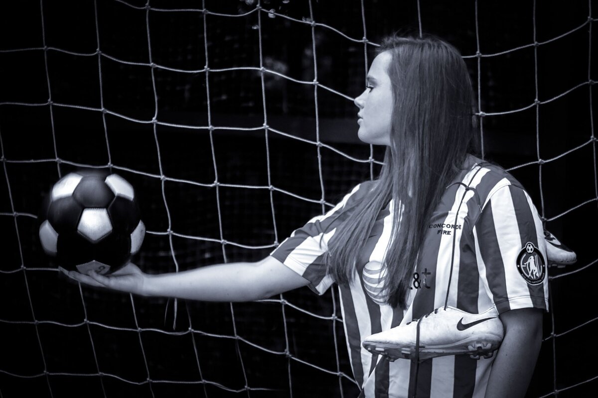 Dramatic black and white senior portrait of a soccer player holding her ball in the goal.