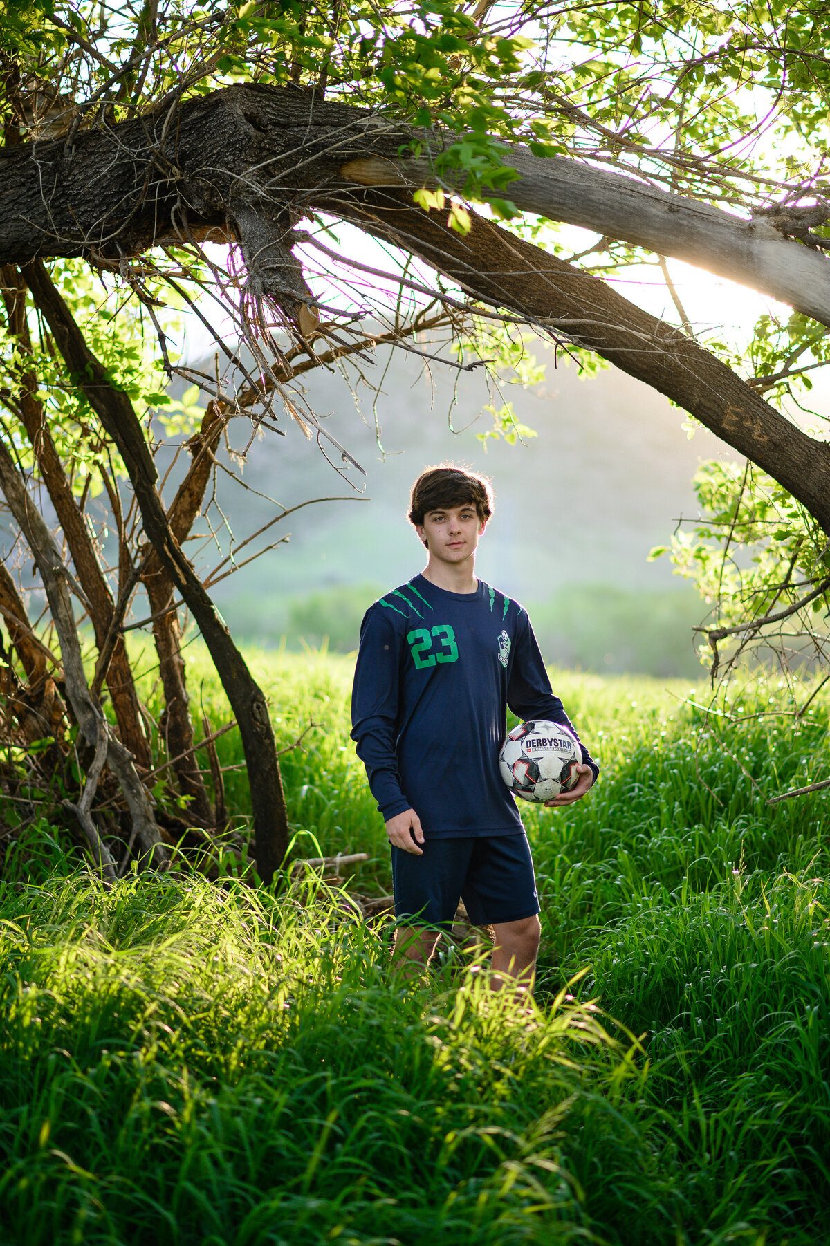 denver senior photographer photographs outdoor senior pictures with young man in his soccer uniform and soccer ball for his senior photos yearbook