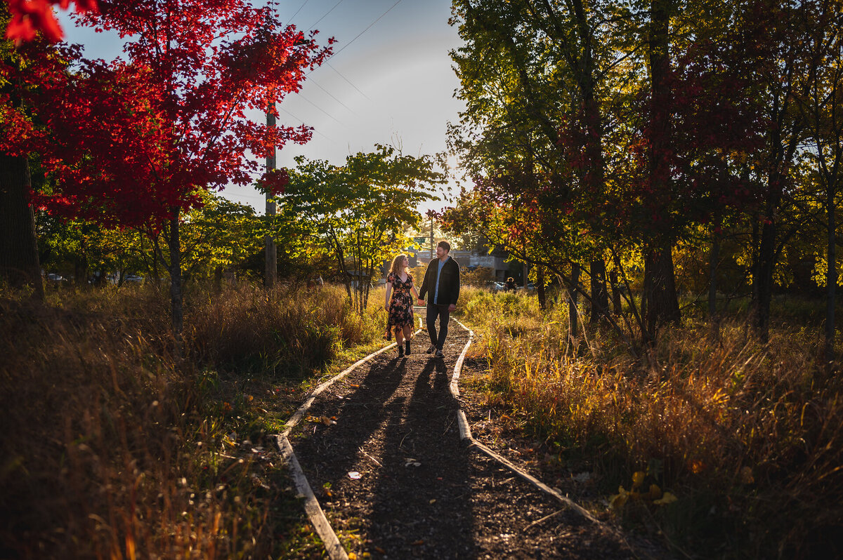 A couple walks down a path in the woods at fall