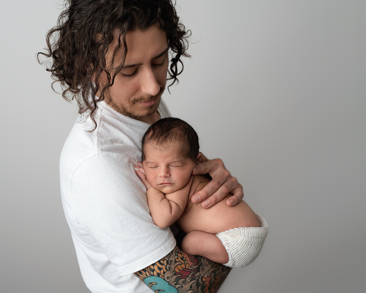 Father holding newborn baby boy during their indoor photography session | Meraki Photographic Creations