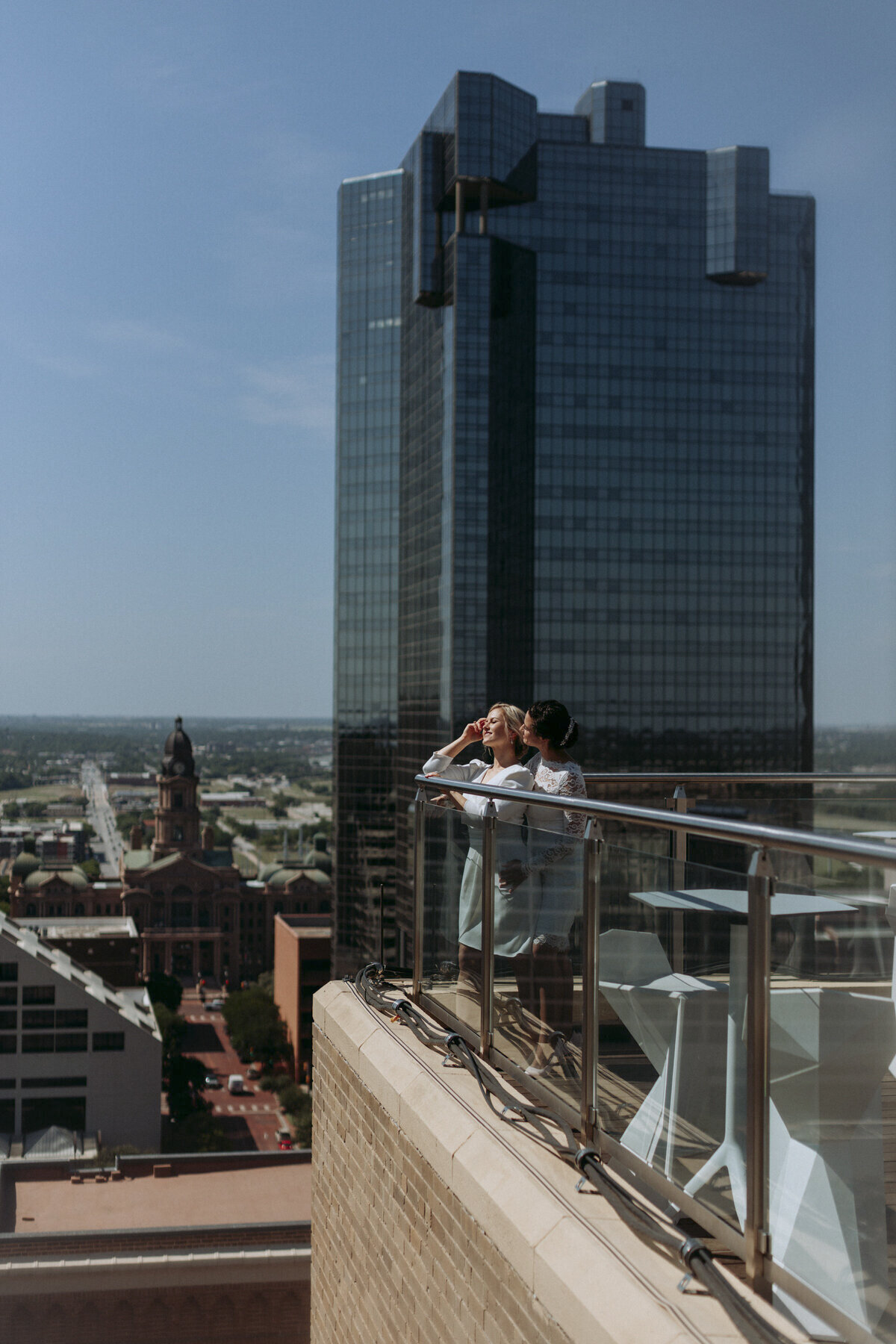 Two brides holding each other and looking out over Downtown Fort worth with the Courthouse in the background