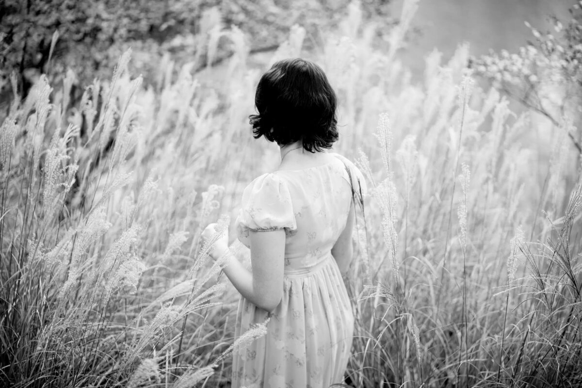 The back of a woman as she walks through a field of grass.