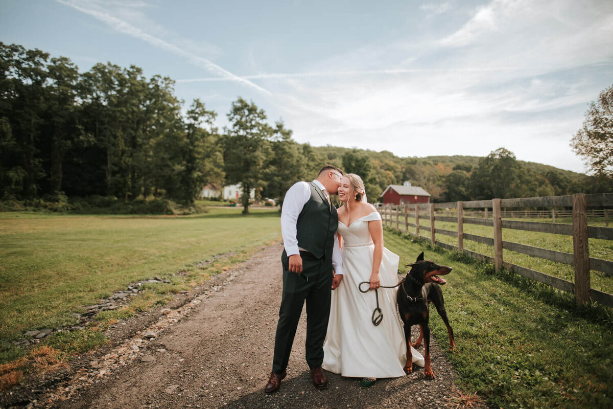 A bride and groom share a joyful moment on a country path, accompanied by their dog.