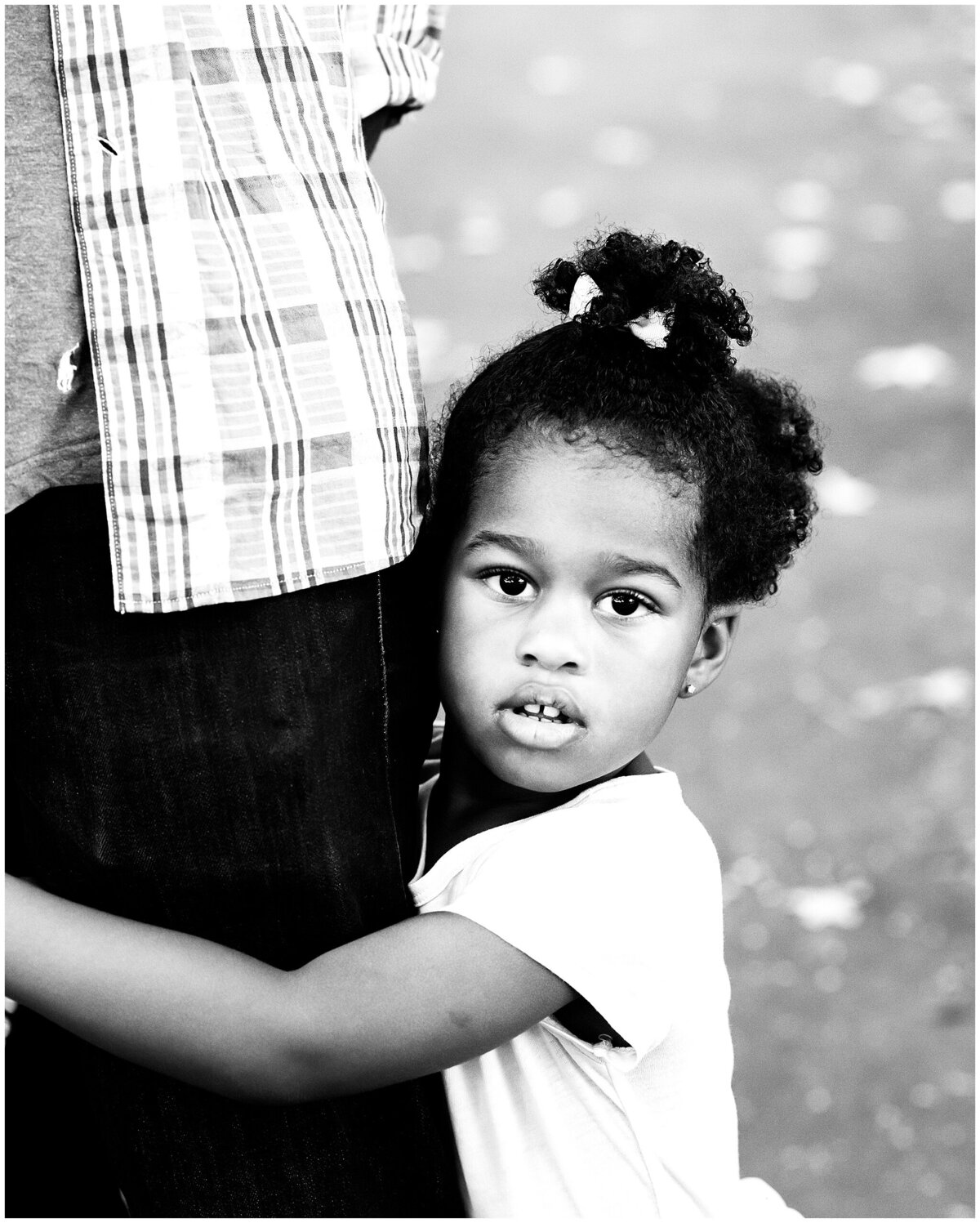2 year old girl holding onto fathers leg in Lincoln Terrace Park portrait session.