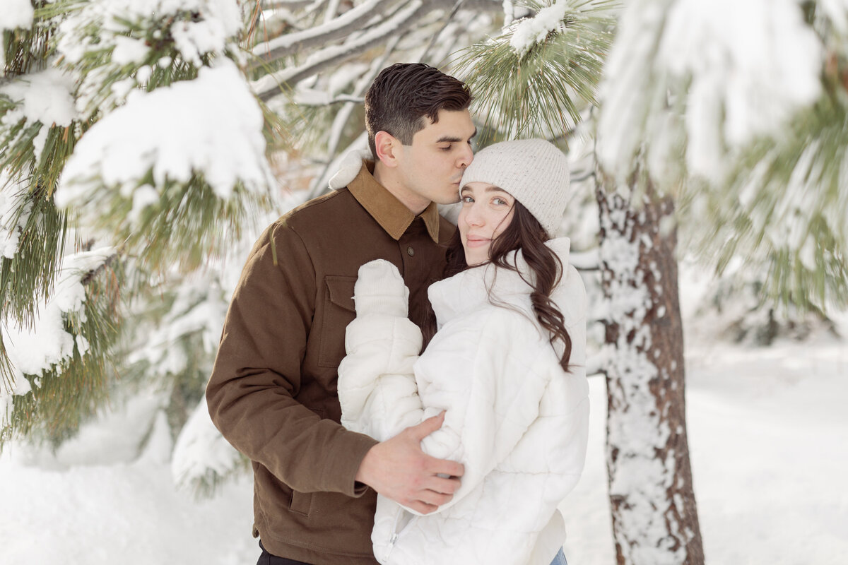 man kissing woman on the forehead in a snowy forest