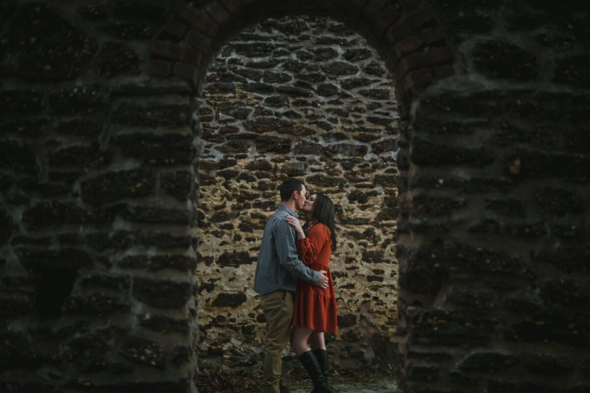 Couple kiss and embrace through the door frame of a stone wall.