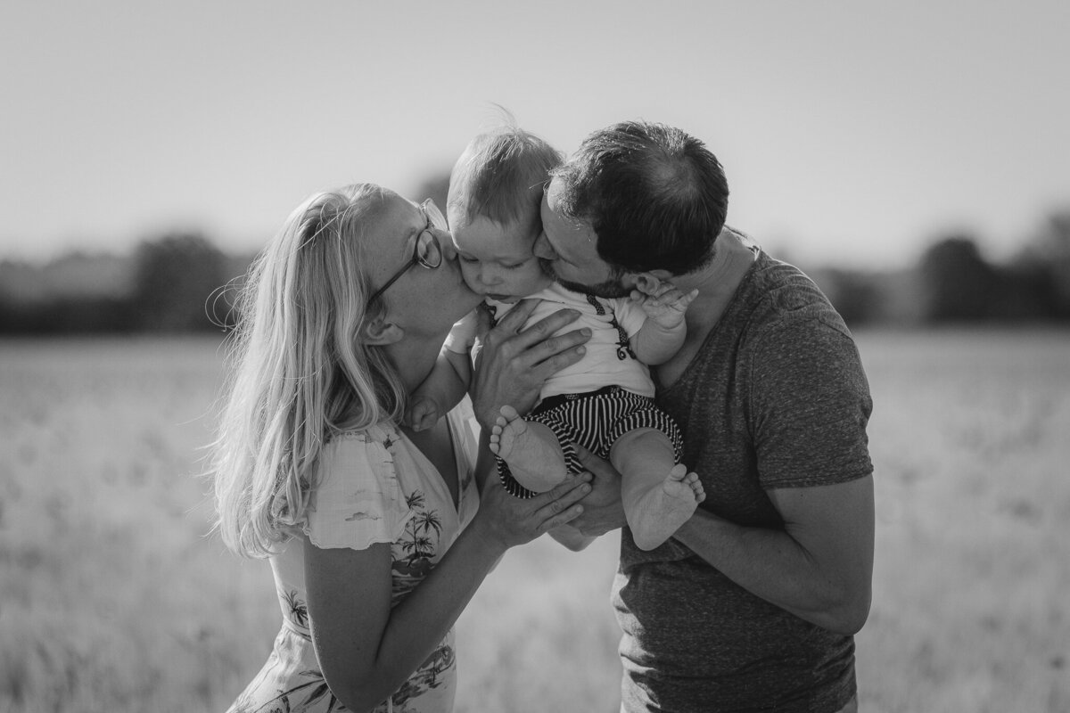 Mom and dad hold their baby up for a simultaneous kiss.