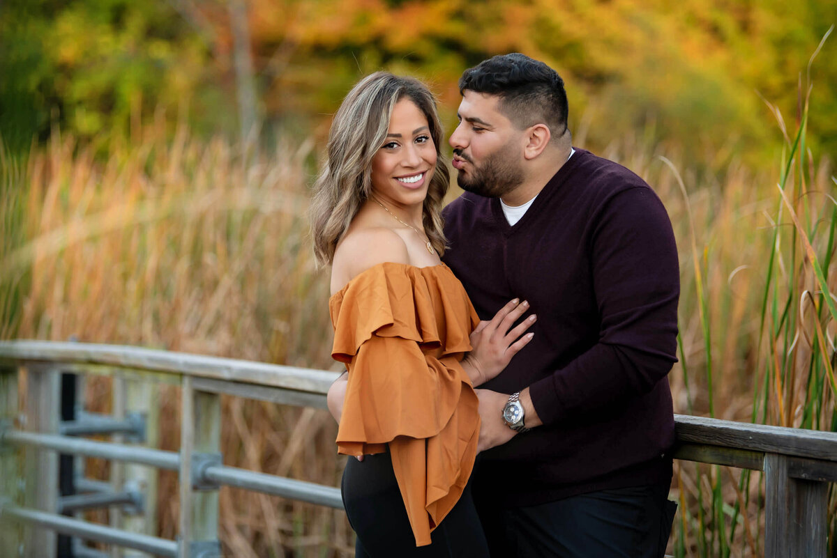 Husband and wife standing on a bridge with their fall family photos in Burlington, On